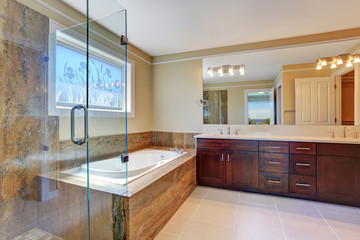 Luxury bathroom interior with large vanity cabinet, glass cabin shower and white bath tub.