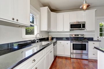 White kitchen room interior with granite counter top and hardwood floor.