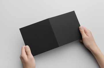 Black Square Bi-Fold Brochure Mock-Up - Male hands holding a black bi-fold on a gray background.