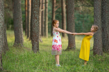 Two little girls for the holding hands in the pine forest.