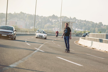 Professional skateboarder riding a skate over a city road bridge, through urban traffic. Free ride skateboards