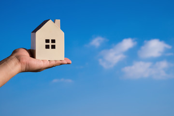 hand holding a house model and a blue sky at background
