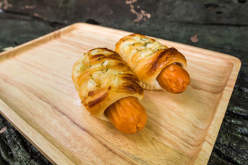 Sausage baked in dough on wooden plate with copy space.