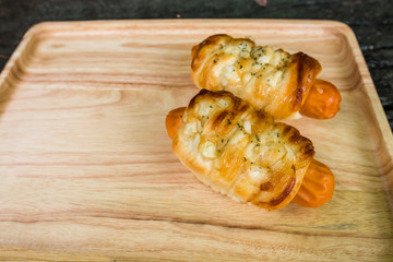 Sausage baked in dough on wooden plate with copy space.
