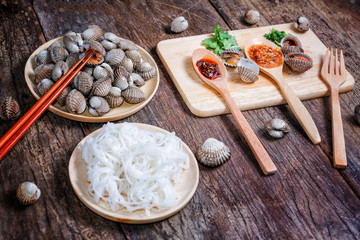 Boiled cockles with rice noodles and tasty seafood sauce on wood table