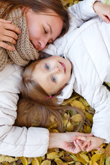 Mother and daughter lying on autumn leaves.