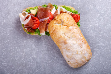 Sandwich with ciabatta, prosciutto,brie cheese and lettuce.On a grey stone background.