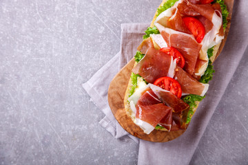 Sandwich with ciabatta, prosciutto,brie cheese and lettuce.on the Board, a grey stone background.