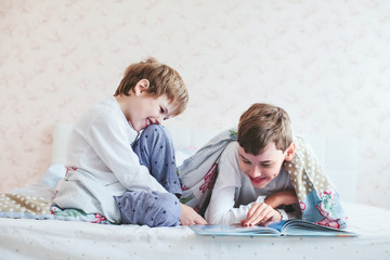 two brothers read a book lying on the bed