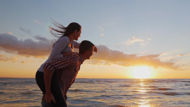 Loving couple having fun on the beach berugu. Girl riding on guy shows his hand forward. Romance, youth and honeymoon. Steadicam slow motion shot