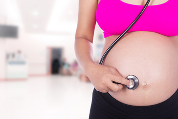 pregnant woman with stethoscope listening belly to baby in hospi