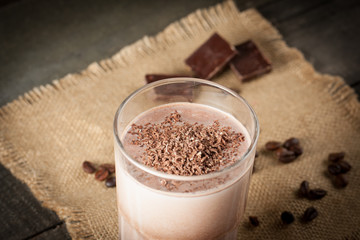 Photo of fresh Made Chocolate Banana Smoothie on a wooden table with coffee and spices. Selective focus. Milkshake. Protein diet. Healthy food concept. Drink, coffee beans, chocolate, 
