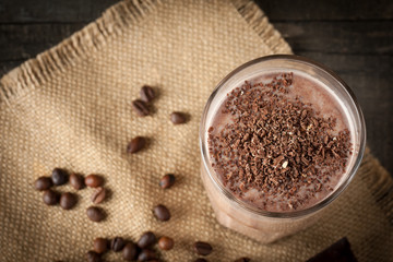 Photo of fresh Made Chocolate Banana Smoothie on a wooden table with coffee and spices. Selective focus. Milkshake. Protein diet. Healthy food concept. Drink, coffee beans, chocolate, 