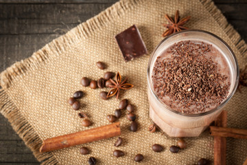 Photo of fresh Made Chocolate Banana Smoothie on a wooden table with coffee and spices. Selective focus. Milkshake. Protein diet. Healthy food concept. Drink, coffee beans, chocolate, 