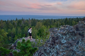 Obraz premium Lady hiker with backpack standing on top of the mountain and enjoying valley view at sunset