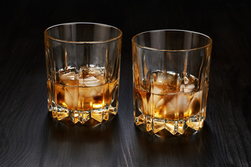 Two glasses of whiskey with ice cubes on dark wooden background