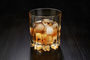 Glass of whiskey with ice cubes on dark wooden background