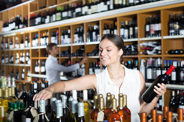 Smiling woman choosing bottle in wine shop