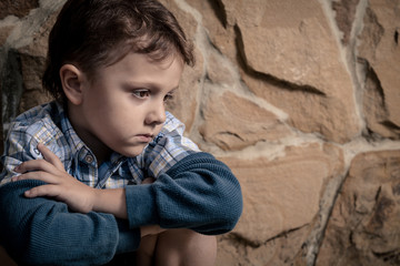 Obraz na płótnie Canvas sad little boy sitting near the wall