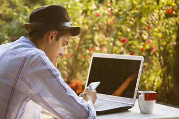 young man with mobile phone and computer drinking coffee outdoors