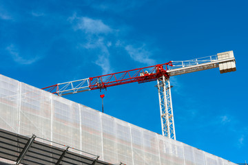 Construction site with red and white crane and a scaffolding on blue sky
