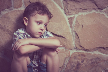 sad little boy sitting near the wall