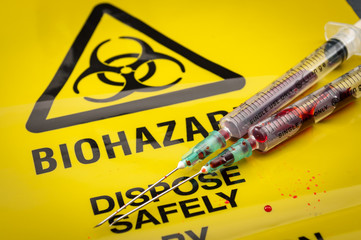Blood filled medical syringes on yellow biohazard bag and spilled biological waste