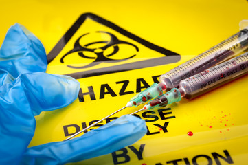 Blood filled syringes and blue medical gloves on yellow biohazard bag and spilled biological waste