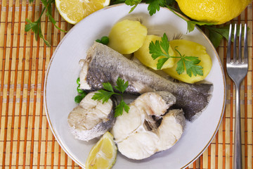 Hake dish with parsley and lemon on wooden background