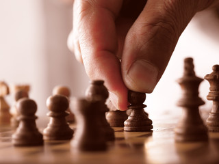 soft focus chess pieces of the fingers of a person making a move gripping a chess piece in a game of intelligence, business strategy planning