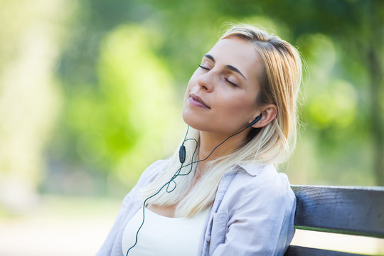 Young happy woman is sitting in park and listening to music. 