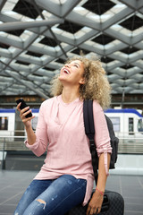 Laughing traveler sitting on suitcase with cellphone