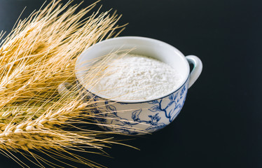 Wheat ears and flour on black background