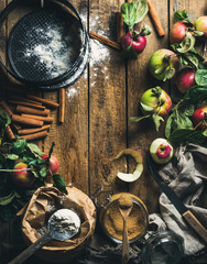 Ingredients for cooking apple pie. Fresh harvest apples with leaves, cinnamon, flour, sugar and baking mold over old rustic wooden background. Top view, copy space in center, vertical