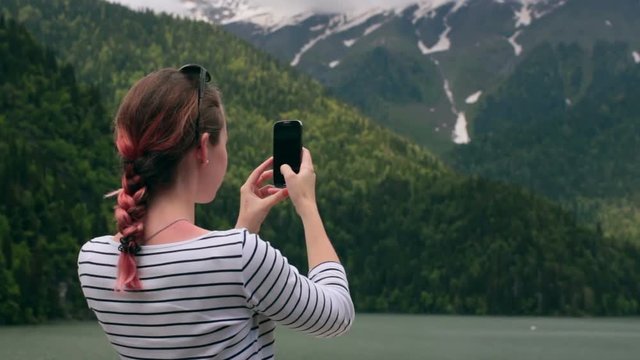 Girl taking photo with smart phone near the mountain lake HD
