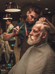 Confident senior man visiting hairstylist in barber shop.
