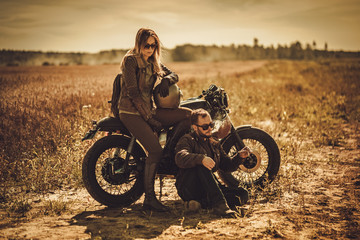 Naklejka na ściany i meble Stylish cafe racer couple on the vintage custom motorcycles in a field.