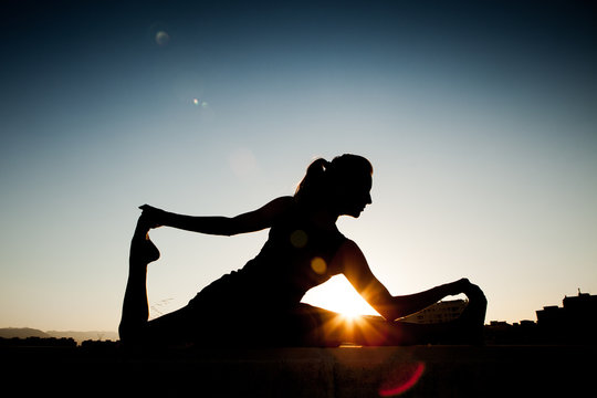 Woman silhouette during a stretching session, with the sun in the background.