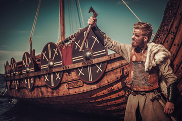 Viking warrior with axes standing near Drakkar on the seashore.
