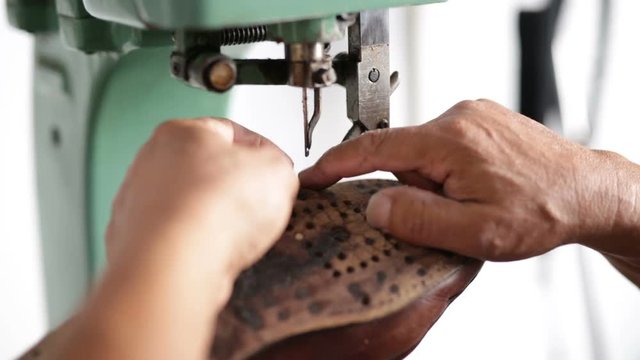 Calzolaio al Lavoro nella sua bottega artigianale. Cucitura suola a fili incrociati alla macchina da cucire manuale. 