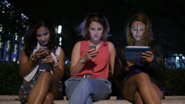 Group of three female friends sat down engaged in their digital devices
