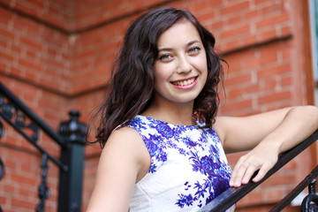 Woman smiling against a backdrop of brick wall holding on to Rails