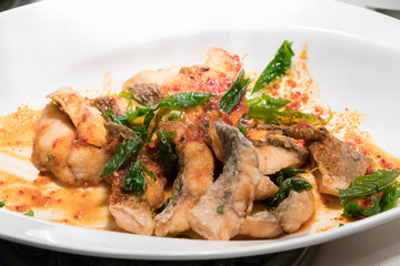 Fried fish in spicy curry sauce on white dish
