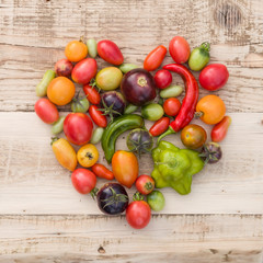 Top view on colorful organic vegetables: tomatoes and paprika in the shape of a heart on wooden background. Healthy food concept.