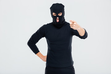 Mad irritated man in balaclava standing and pointing on you