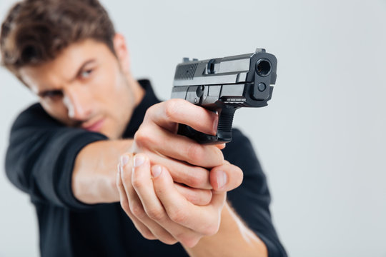 Serious young man standing and aiming with gun
