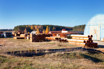 landscape of metal round warehouse and pvc orange plastic pipe stacks for plumbing in front the autumn forest