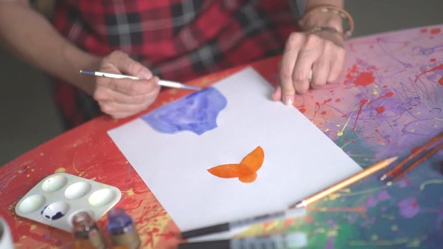 Drawing watercolor. Female artist paints watercolors silhouette. Blue watercolor paint. Orange paint. The artist at work. Drawing lessons