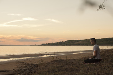 Yoga man sitting on the beach at sunset