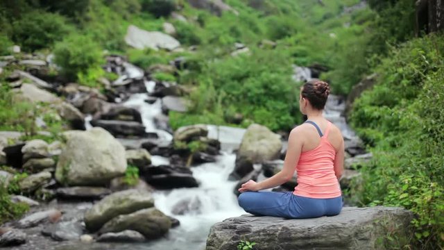 Woman meditating at tropical waterfall in Lotus pose Padmasana
